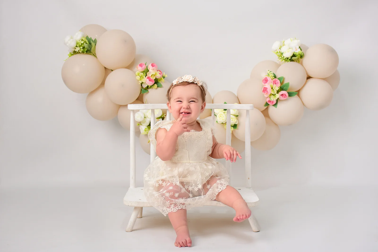 Bebé en una hamaca blanca con globos beige y flores