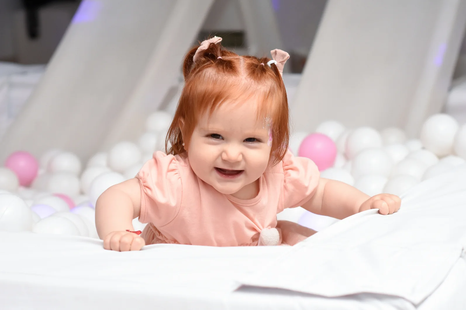 Bebé apoyada sobre una manta blanca rodeada de globos pastel