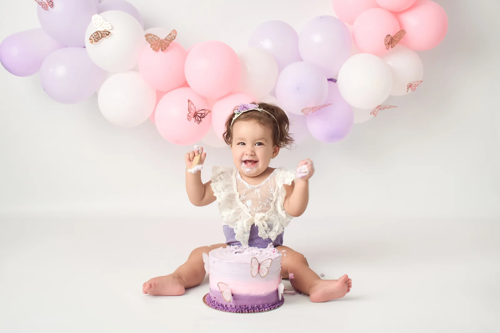 Bebé jugando con una torta violeta bajo globos pastel