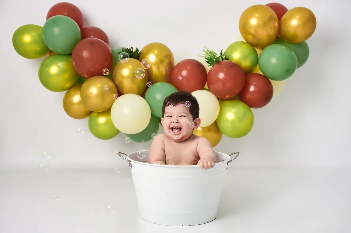 Bebé riendo en el baño de burbujas rodeado de globos verdes y dorados