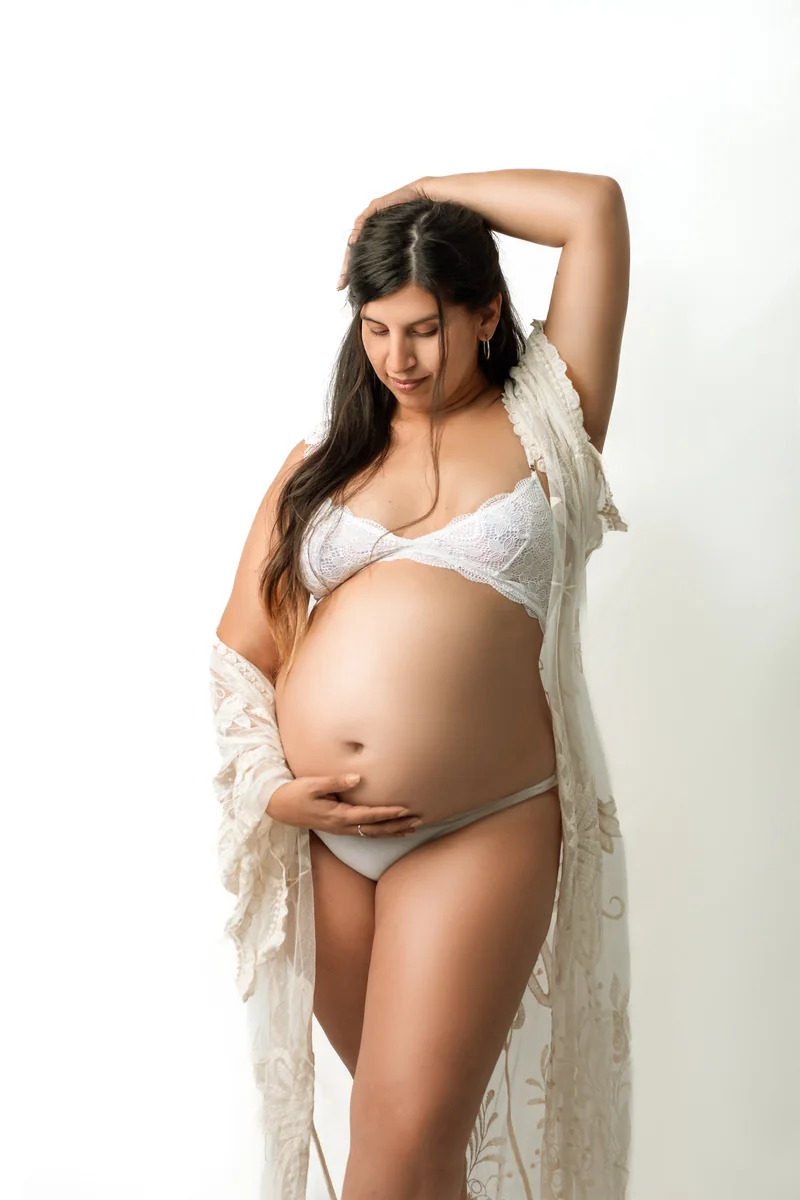 Futura mamá con vestido de encaje sosteniendo su panza en estudio