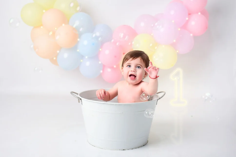 Bebé dentro de una bañera con burbujas y globos de colores pastel