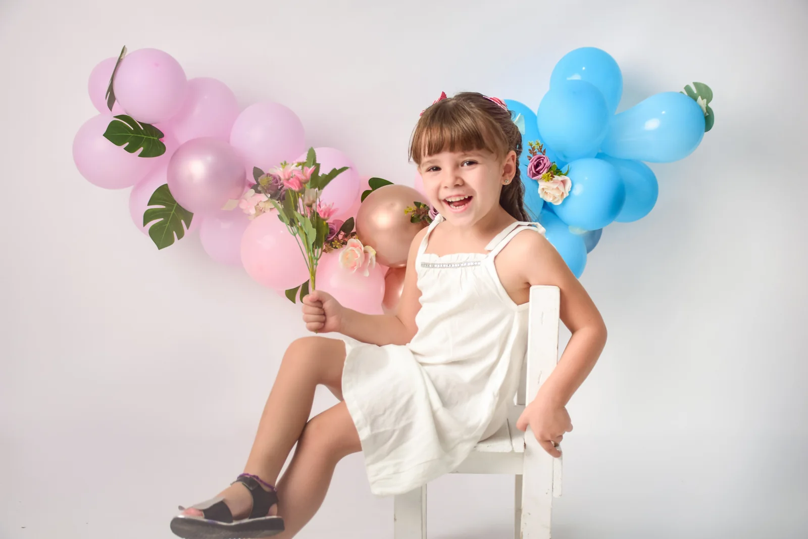 Nena con un ramo de flores delante de globos rosados y celestes